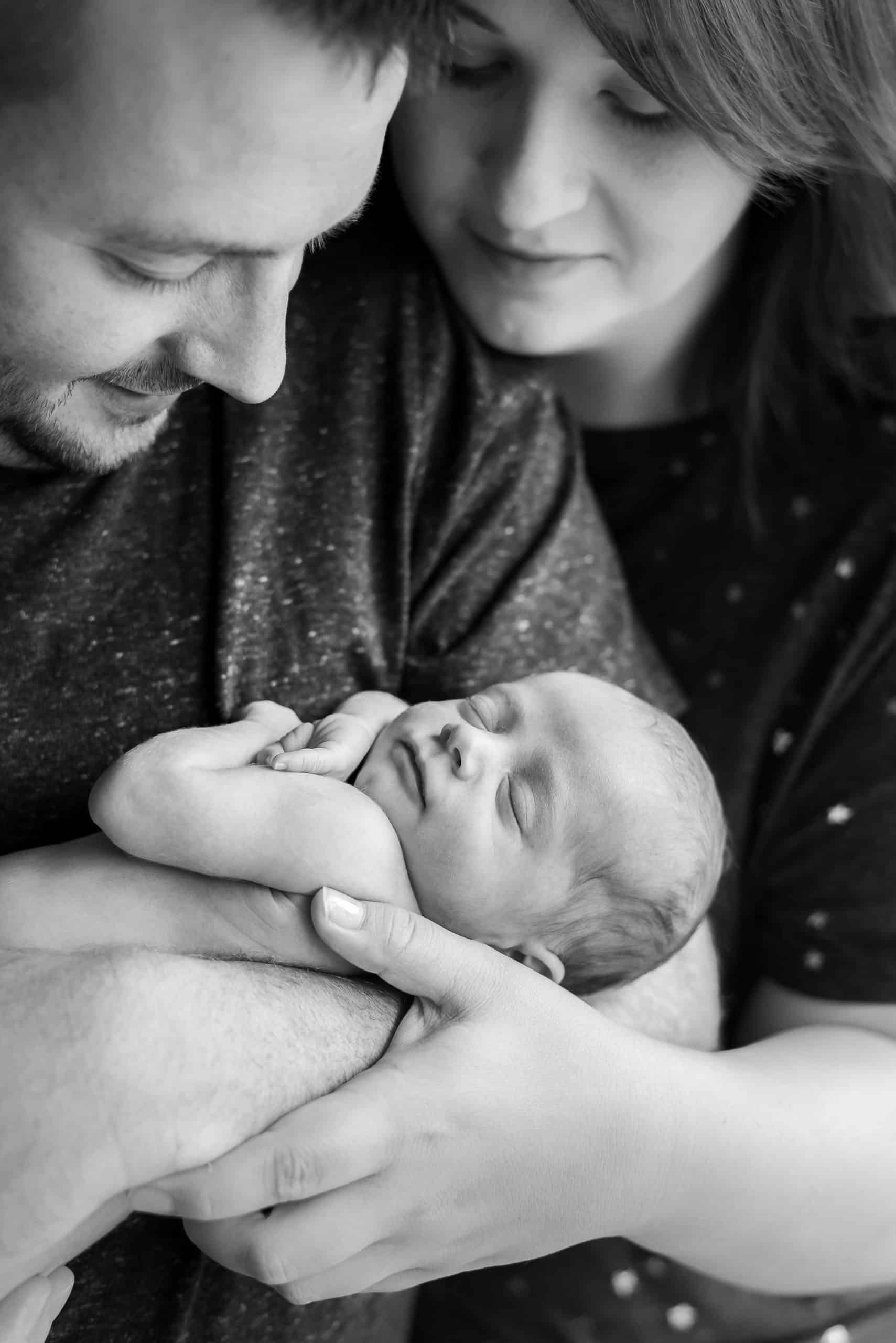 black and white photo on newborn baby and mum and dad for their newbron baby photoshoot. Dad is holding the baby and mum has her arm around them