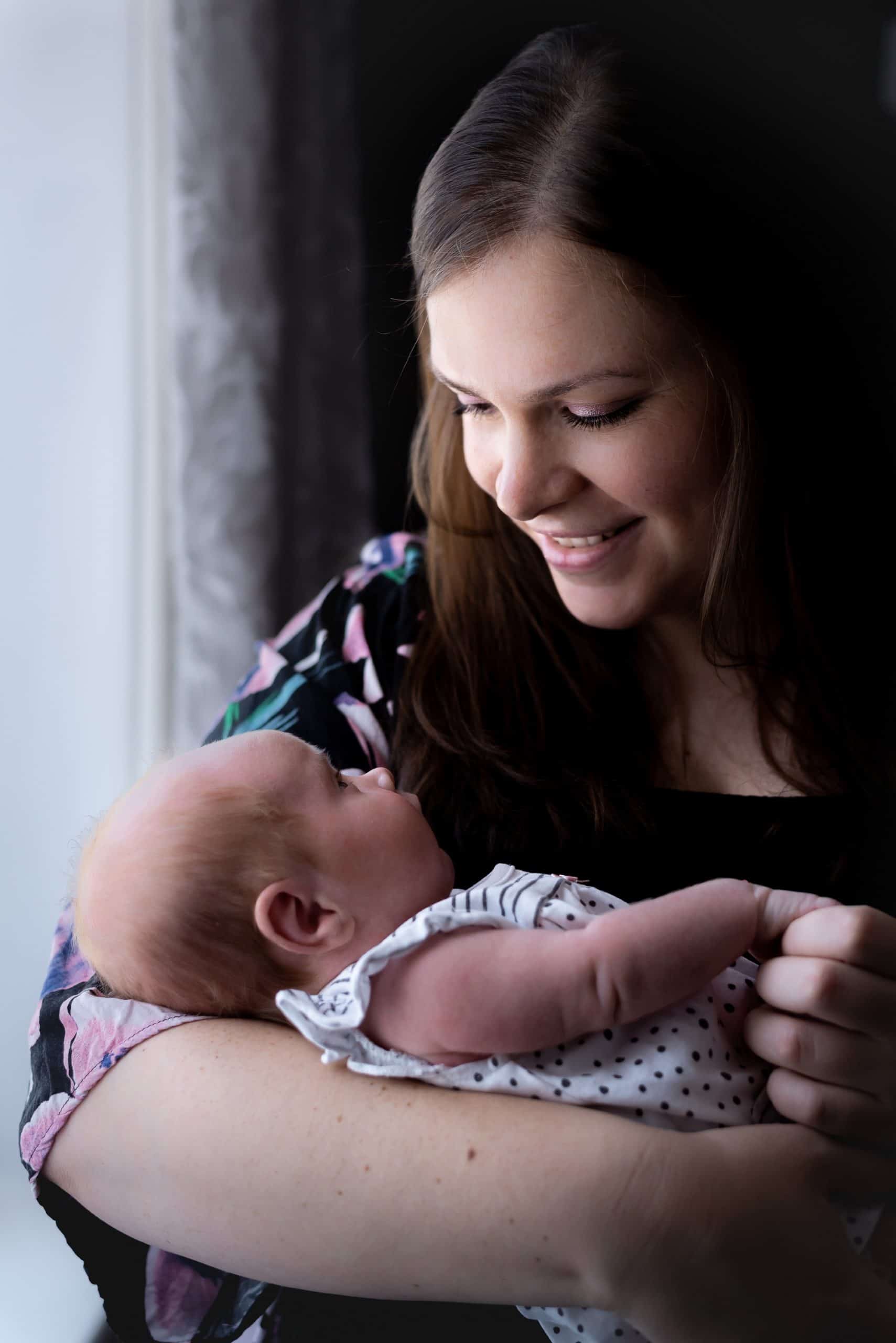 mother and her newborn baby stood by the window for some natural light family photos