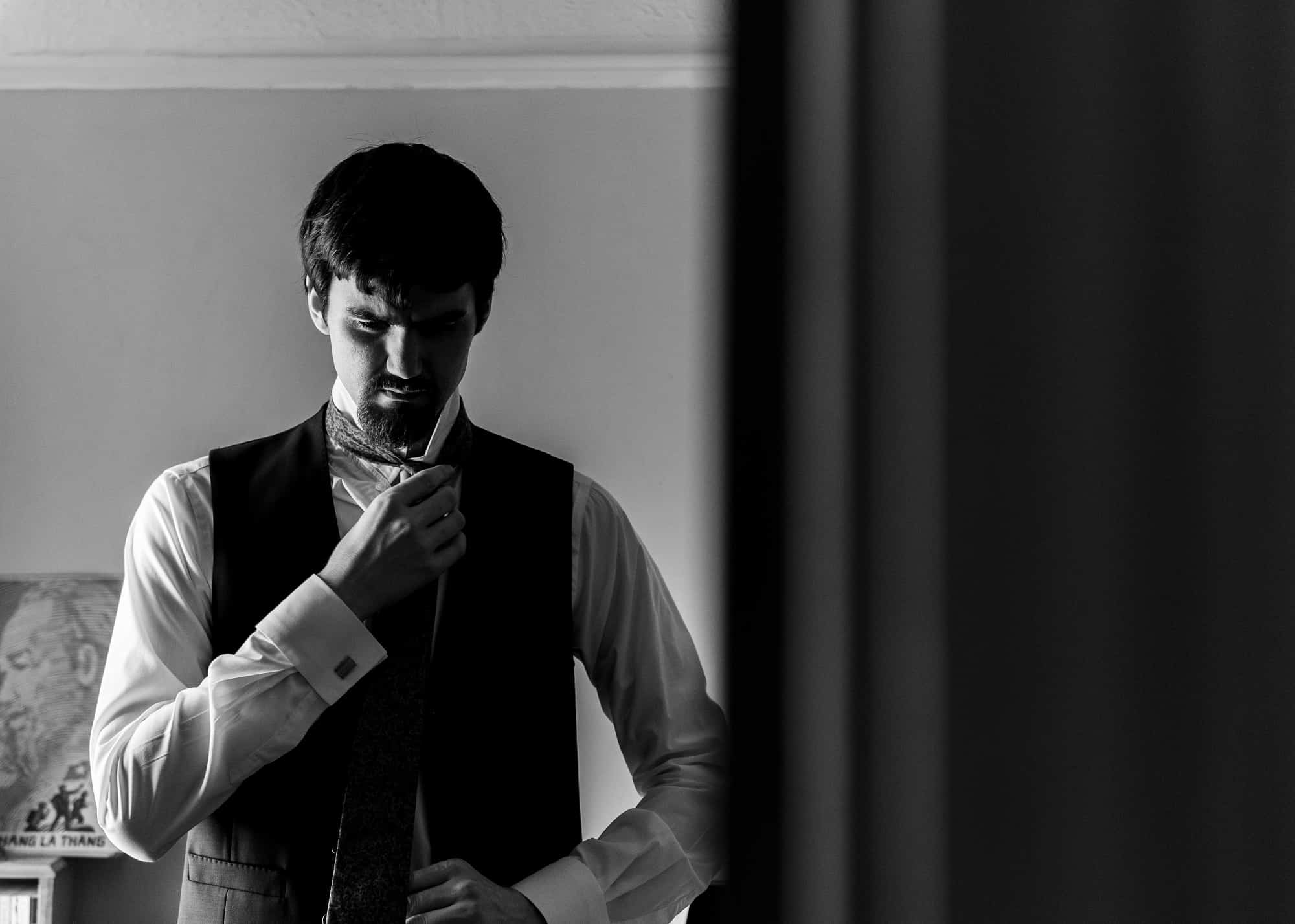black and white of groom getting ready, adjusting his tie